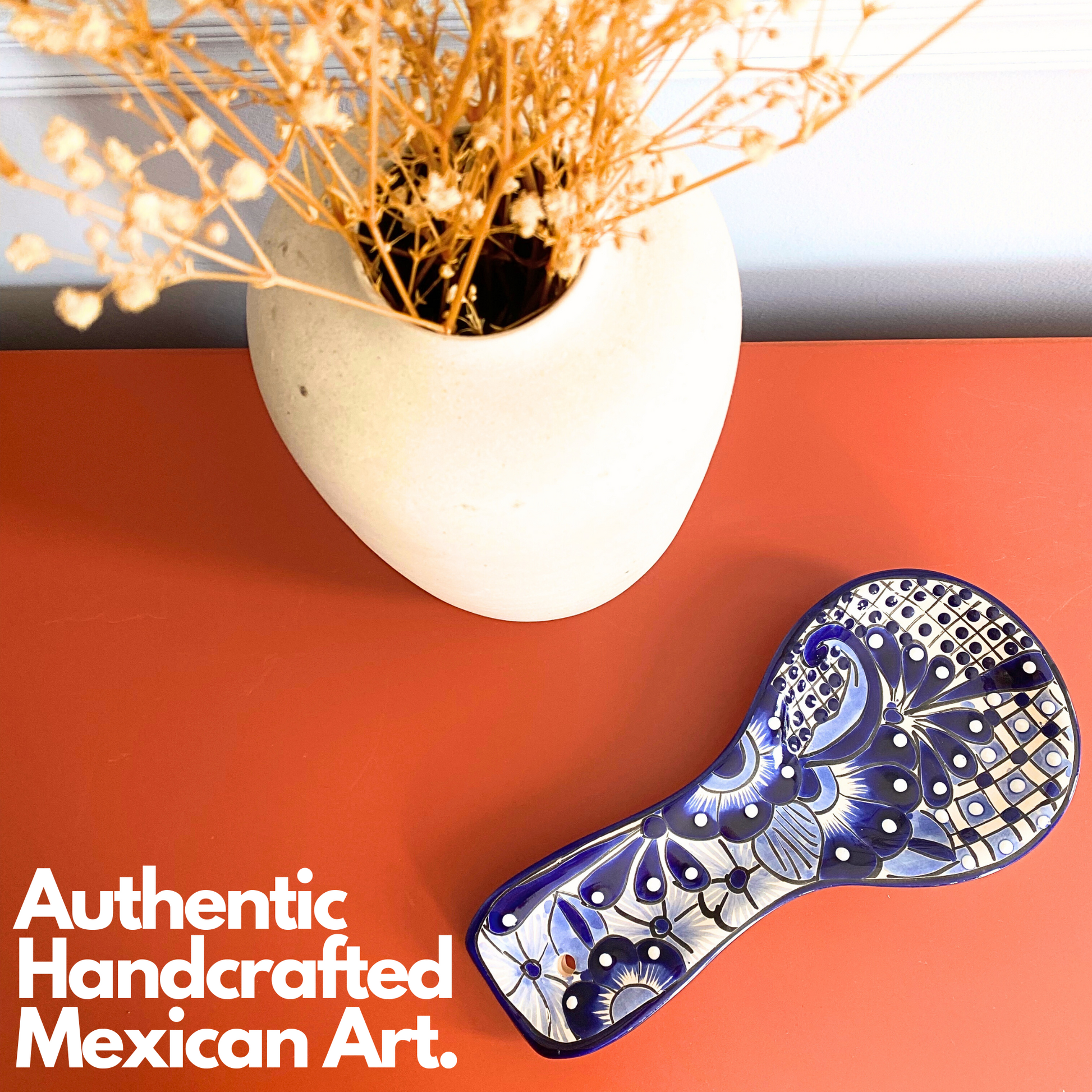 Blue and white Talavera-style ceramic spoon rest, hand-painted in Mexico — styled on a terracotta surface beside a vase with dried flowers