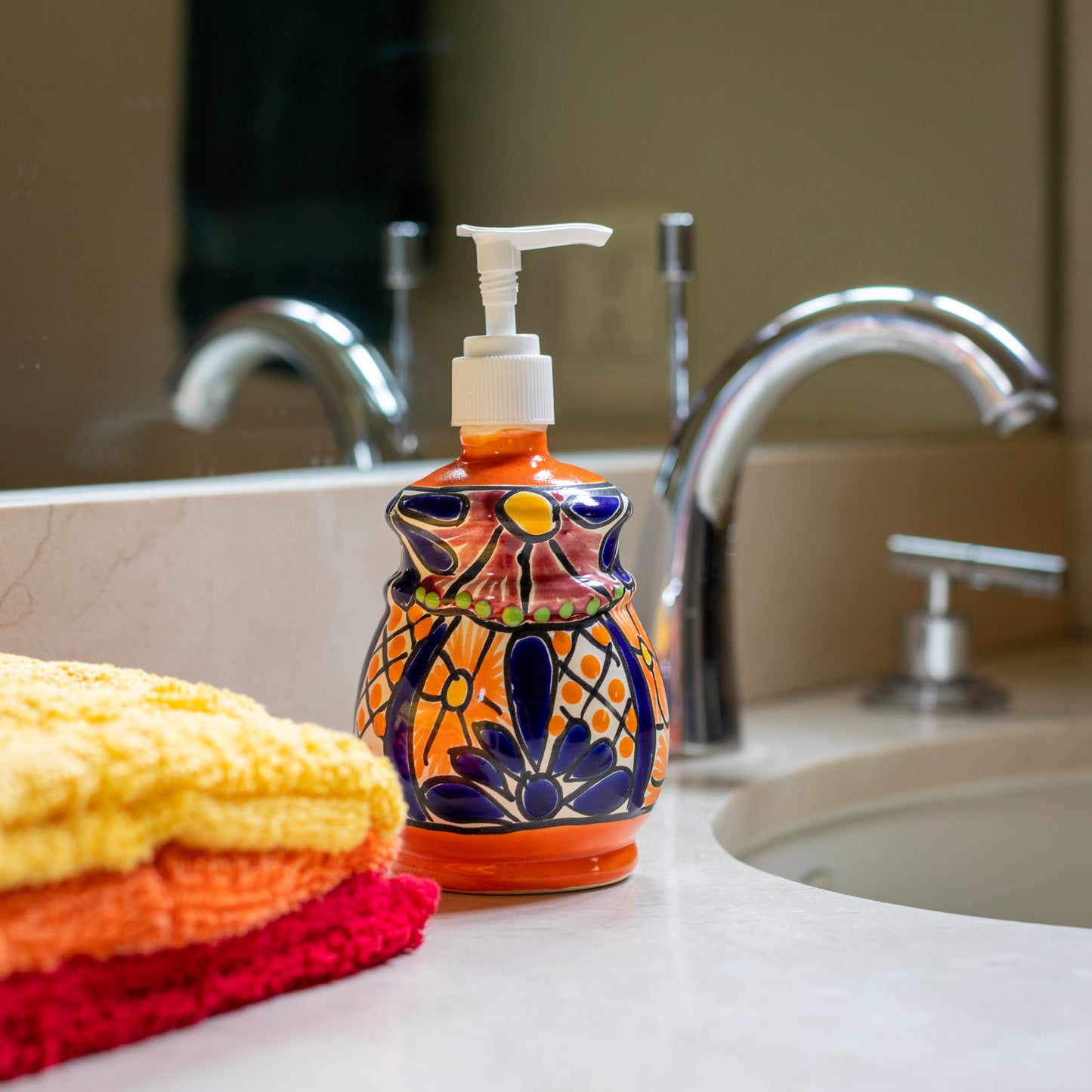 A multicolored, bell design, hand-painted Talavera ceramic soap dispenser sourced from skilled Mexican artisans. on the bathroom sink