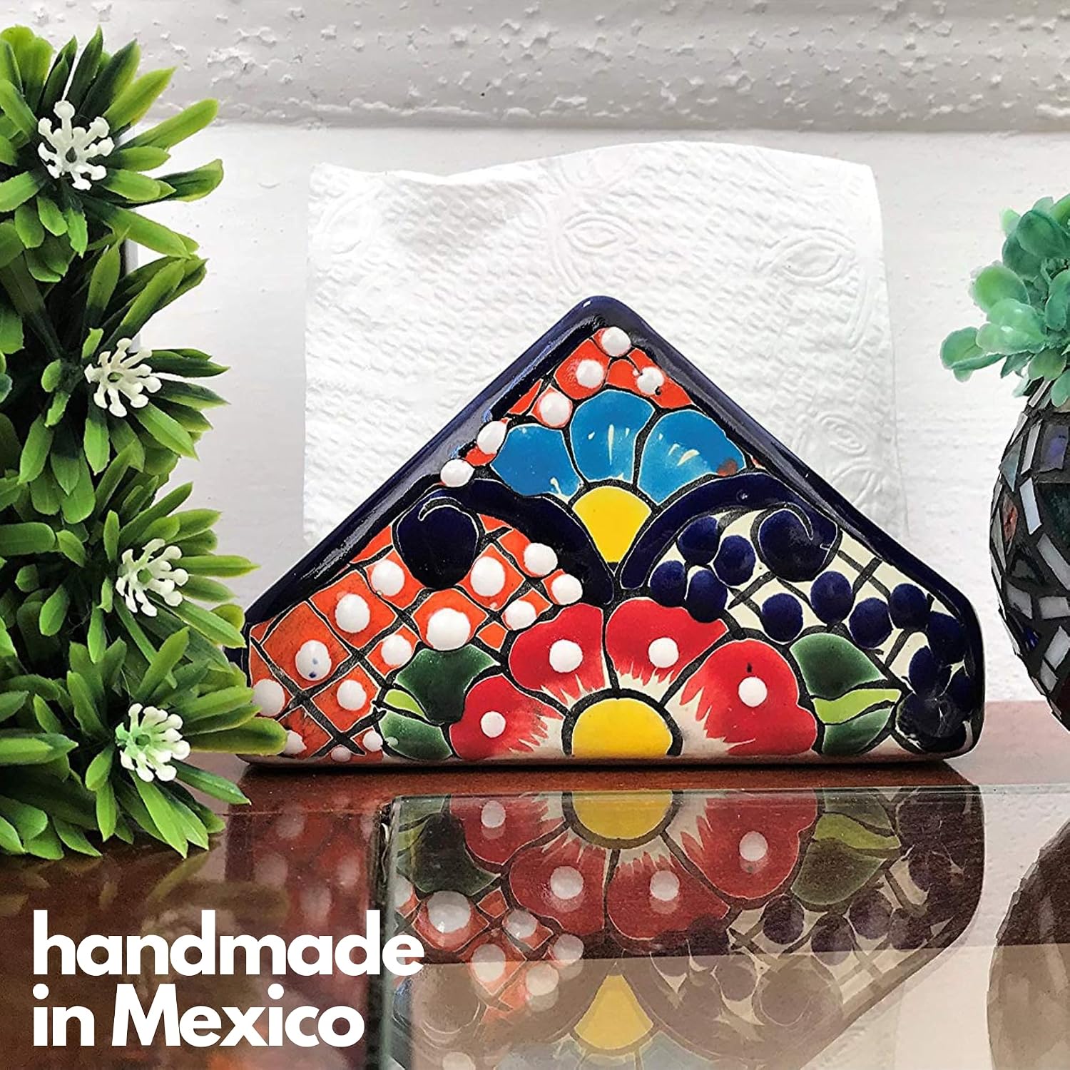 Colorful Talavera-style Mexican ceramic napkin holder, hand-painted in Mexico — styled on a glass table beside green plants