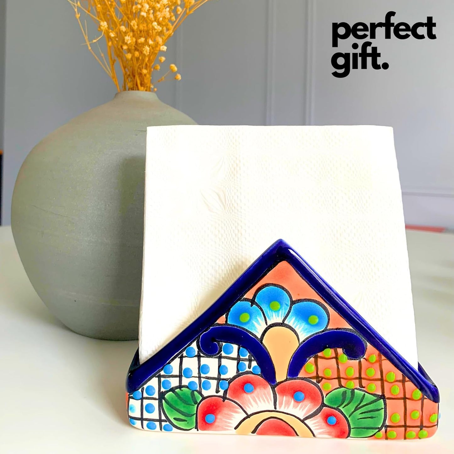 Colorful Talavera-style Mexican ceramic napkin holder, hand-painted in Mexico — holding a folded napkin beside a stone vase