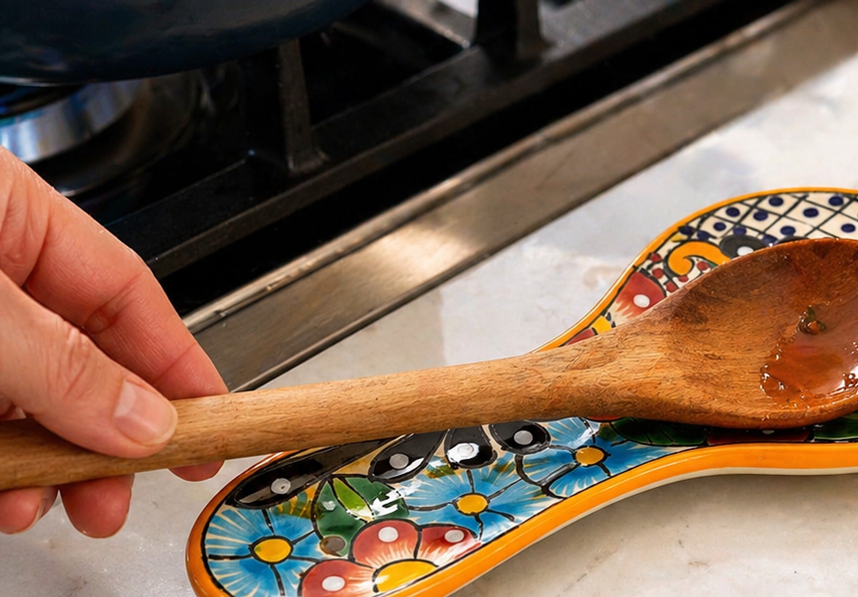 Hand-painted Mexican ceramic spoon rest holding a wooden spoon on a kitchen counter